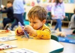 A child practicing fine motor skills by threading beads in a Montessori classroom.